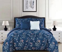 a bed with blue comforter and pillows in a white room next to two lamps