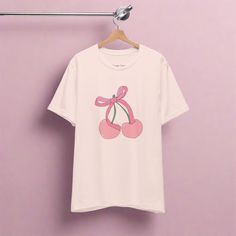 Embrace the sweetness of the current coquette trend with this adorable design featuring two plump pink cherries adorned with a cute, pink bow. Perfect for adding a playful touch to your wardrobe, this t-shirt combines whimsy with style, making it an ideal choice for any fashion-forward individual. Whether you're strolling through the city streets or enjoying a casual outing with friends, the "Cherry Bowby" tee is sure to turn heads and spark conversations. Indulge in the irresistible allure of o Trendy Summer T-shirt With Bow, Pink Crew Neck T-shirt With Cute Design, Casual Summer T-shirt With Pink Bow, Casual Short Sleeve T-shirt With Pink Bow, Pink Cotton T-shirt With Cherry Print, Pink Kawaii T-shirt For Summer, Kawaii Pink Summer T-shirt, Pink Casual T-shirt With Cute Design, Casual Pink T-shirt With Cute Design