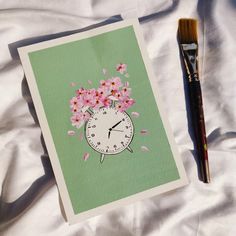 a clock with pink flowers on it next to a paintbrush and paper work piece