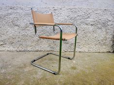 a tan leather chair sitting in front of a white stucco wall with a metal frame