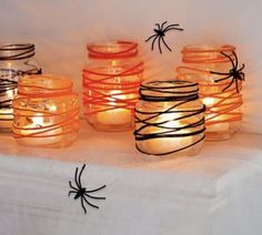 several jars with candles wrapped in black string and spider webs on the lids, sitting on a white surface