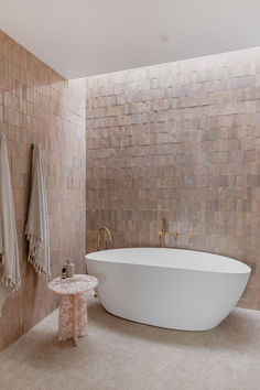 a bath tub sitting next to a white table in a room with tile walls and floor