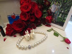 two white rabbits on a pearl bracelet with roses in the background and a card that says happy valentine's day