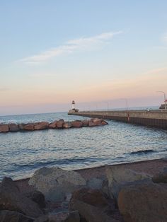 there is a large body of water next to the shore with rocks on it and a light house in the distance