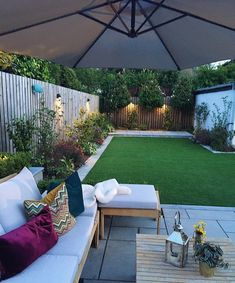 an outdoor patio with white couches and green grass in the back yard, next to a wooden table