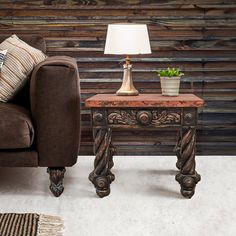 a brown couch sitting next to a lamp on top of a table in front of a wooden wall