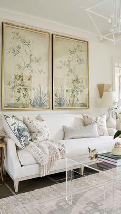 a living room with white furniture and paintings on the wall above it's coffee table