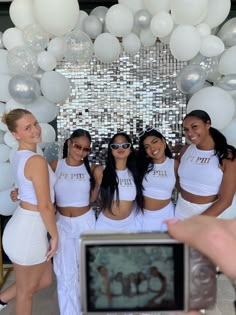 a group of young women standing next to each other in front of white balloons and disco balls