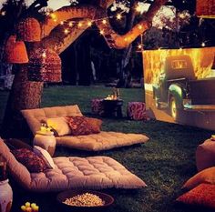 an outdoor movie is set up in the grass with lights strung over it and pillows on the ground