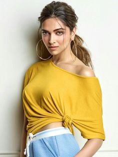 a woman leaning against a wall with her hands on her hips wearing shorts and a yellow top