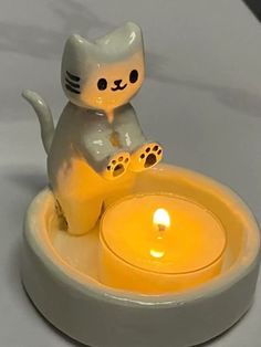 a white cat figurine sitting on top of a candle holder with a lit candle in it