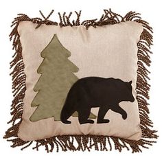 a black bear is standing next to a christmas tree on a beige pillow with fringe trim