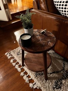 a small table with a candle on it in front of a brown leather couch and rug