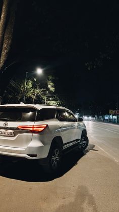 a white suv is parked on the side of the road at night with its lights on