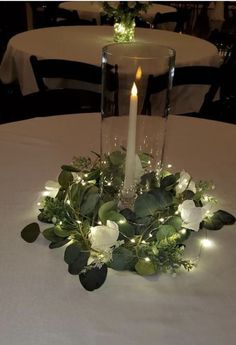 a candle is lit on top of a table with flowers and greenery around it