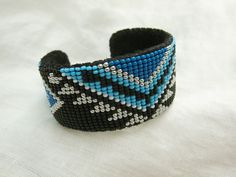 a blue and black beaded bracelet on a white cloth with an arrow in the middle