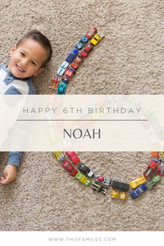 a young boy laying on the floor next to a happy 6th birthday sign with toy cars