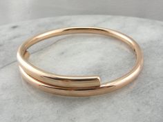 "This can easily be worn alone, but would look great stacked with other bracelets as well. The bangle is round, crafted of a solid, 5.5mm wide rose gold, slightly domed on top and doubled over itself to create a bypass. This is such a simple design, and so pretty on the wrist! Metal: 9Ct Rose Gold Width: 11.6 mm (at widest point) Inside Diameter: 3 Inches Marks: \"9Ct 9Ct\" Stamped on the inside SKU #: Q0JV36-P Each piece has been identified and graded by a Graduate Gemologist who has been certi Eternity Bands, So Pretty, Bangle Bracelet, Simple Design, Simple Designs, Bangle Bracelets, Gold Jewelry, Gold Bracelet, Bangles