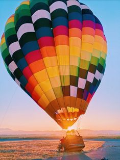 a large hot air balloon flying over a lake in the middle of the desert at sunset