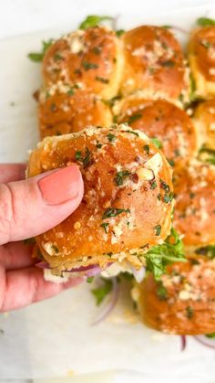 a person is holding up a sandwich with meat and herbs on it, in front of other bread rolls