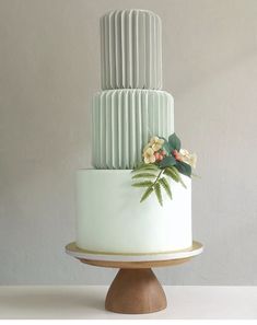 a three tiered cake with white icing and greenery on top, sitting on a wooden stand