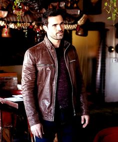 a man wearing a brown leather jacket standing in a room