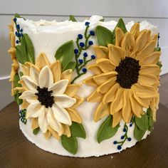 a cake decorated with sunflowers and leaves on top of a wooden table next to a wall