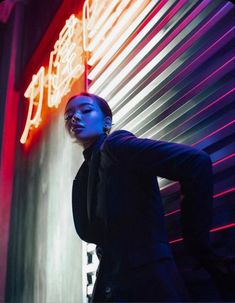 a woman standing in front of a neon sign with her hands on her head and looking off to the side