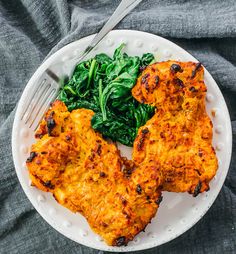 two pieces of chicken on a plate with spinach and a fork next to it