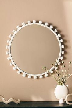 a white vase sitting on top of a wooden table next to a round shaped mirror