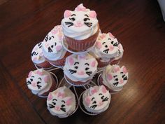 a stack of cupcakes with white frosting and cat faces on them sitting on top of a wooden table