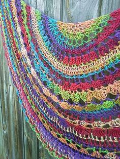 a multicolored crocheted shawl hanging on a wooden fence