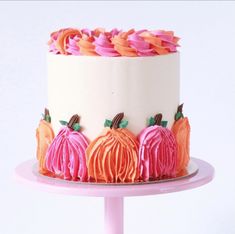 a white cake with pink frosting and pumpkins on the top is sitting on a plate