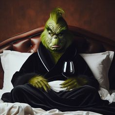 a green creature sitting on top of a bed next to a glass of wine in his hand