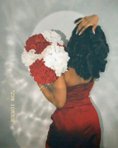 a woman in a red dress holding a bouquet of flowers with her hands behind her head