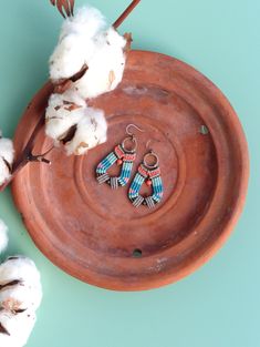 two pairs of earrings sitting on top of a brown plate next to cotton floss