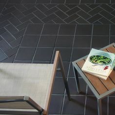 a table with a book on it and two chairs next to it in front of a tile floor