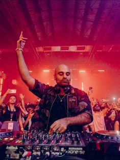 a dj mixing in front of a large group of people at a concert with their hands up