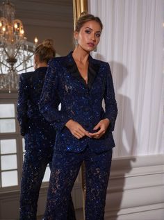 a woman standing in front of a mirror wearing a blue suit with sequins