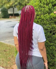 a woman with long red braids standing in front of some bushes and looking at the ground