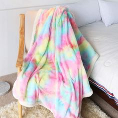 a bed with a colorful blanket on top of it next to a white pillow and chair