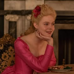 a woman in a pink dress sitting at a table with a plate of food on it