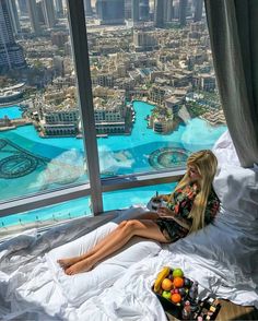 a woman sitting on top of a bed in front of a window overlooking the city