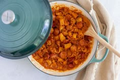 a large pot filled with food on top of a white tablecloth next to a wooden spoon