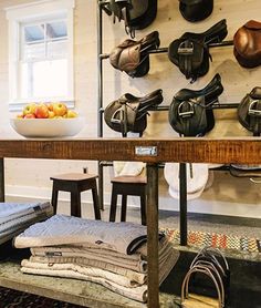 there are many saddles hanging on the wall in this room, and one has a bowl of fruit