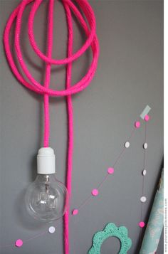 a pink rope with a light bulb attached to it on a gray wall next to confetti