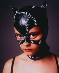 a woman wearing a black cat mask with white letters on it