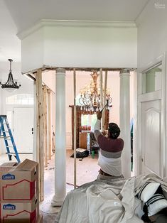 a man standing on top of a bed in a room under construction next to a chandelier