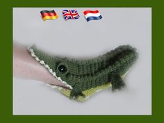 a hand is holding a small crocheted alligator in front of the flag of britain