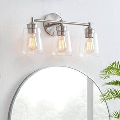 three light bathroom fixture with clear glass shades and round mirror in front of white wall